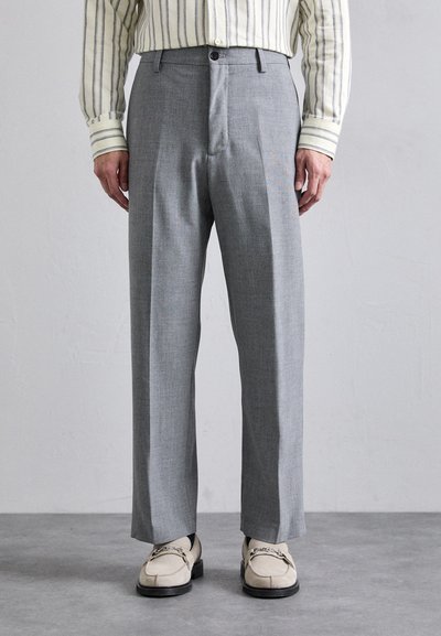 Pantaloni grigi su misura con una trama texturizzata, caratterizzati da una parte anteriore piatta, due tasche laterali e una vestibilità rilassata. Abbinati a scarpe di colore chiaro.