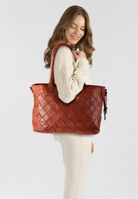 Borsa tote in pelle marrone con un design intrecciato, caratterizzata da motivi a rombo, doppi manici e chiusura con zip. Tessuto liscio, interno spazioso.