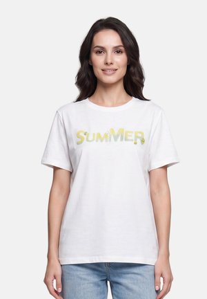 Donna con capelli scuri che indossa una maglietta bianca con la parola "SUMMER" in lettere gialle, abbinata a jeans azzurri, in piedi davanti a uno sfondo bianco.