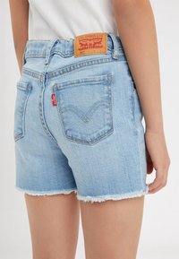 Jasnoniebieskie szorty jeansowe z postrzępionym dołem, z tylnymi kieszeniami i skórzaną naszywką Levi's z czerwonym logo.