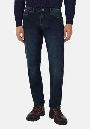 Donkerblauwe denim jeans met een slim fit, vijf zakken en een rits. Draagt met bruin gevlochten laarzen en een kabelgebreid trui.