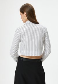 Camicia bianca tagliata con sottili righe nere, maniche lunghe e colletto. Abbinata a pantaloni neri a vita alta. Texture del tessuto liscia.