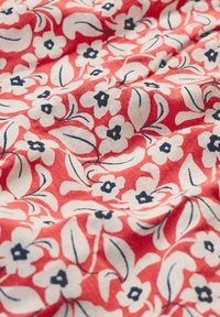 Țesătură roșie cu un model floral, având flori albe și accente de albastru închis, combinate cu frunze delicate verzi și un aspect texturat.