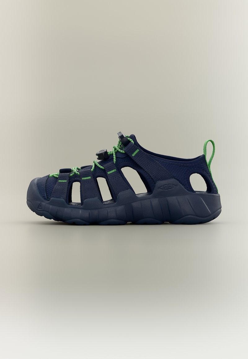 Ανοιχτόσολη πέδιλο σε ναυτικό μπλε με πράσινα κορδόνια, ενισχυμένο καπάκι δακτύλων, μαξιλαρωμένη σόλα και λουράκι στη φτέρνα σε ουδέτερο φόντο.