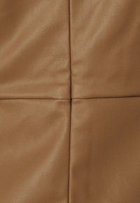 Gros plan de quatre panneaux en cuir fauve cousus ensemble, montrant le grain naturel et de légères plis dans le matériau.