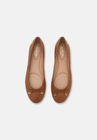 Hnědé kožené baletky s kulatou špičkou, mašlí vpředu a zlatými kovovými detaily poblíž paty.
