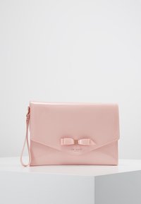 Pochette en cuir verni rose avec rabat à rabat, détail nœud décoratif et une sangle pour poignet. Présente un logo métallique à l'avant.