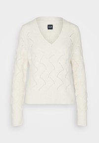 Pull en maille blanche avec un col en V, présentant un motif en vagues et des poignets côtelés. Confectionné dans un matériau doux et texturé pour le confort.