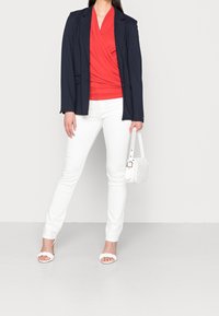 Laivastonsininen bleiseri, punainen kietaisutoppi, valkoiset kapeat farkut ja valkoinen käsilaukku. Valkoiset avokkaat, joissa on aallotettu reuna. Kaikki vaatekappaleet ovat istuvia.