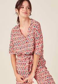 Vestido a rayas rojas y blancas con mangas cortas, un cuello y un lazo en la cintura. La tela presenta un diseño repetido en forma de gota en azul y rosa.