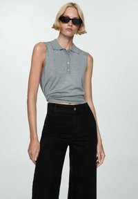 Gray sleeveless polo top with buttons and a ribbed hem, paired with high-waisted black wide-leg jeans. Model wearing black sunglasses.