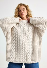 Chunky striktrøje i cremet beige med kabelmønstre, ribbede ærmer og en afslappet pasform med rund hals.