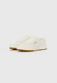 Pair of off-white Skechers sneakers with gum soles, green and red logo on side, and laces, shown against a plain white background.