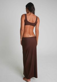 Bruin twee-delig outfit bestaande uit een aansluitende bralette en een lange, vloeiende rok. De stof is glad met een lichte glans en minimale accenten.