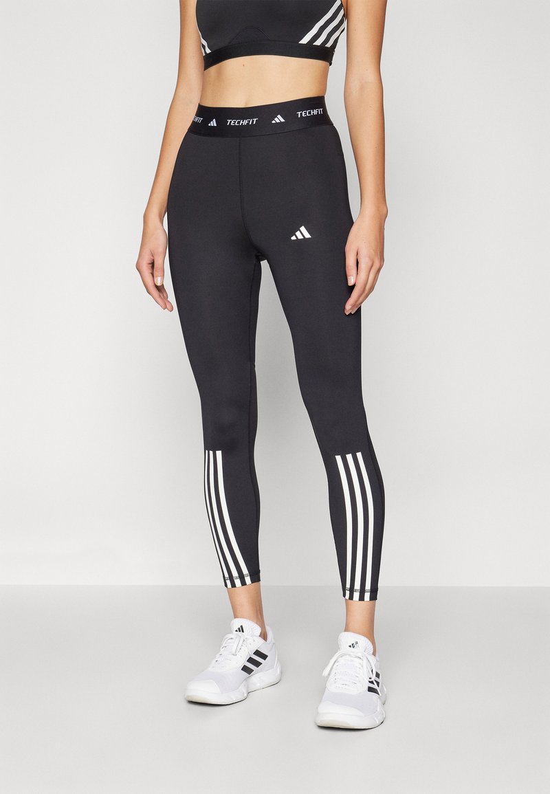 Zwarte legging met witte strepen aan de zijkanten, met een "TECHFIT" tailleband en het Adidas-logo. Gemaakt van rekbaar, nauwsluitend materiaal.