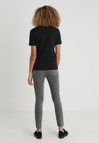 Schwarzes T-Shirt mit kurzen Ärmeln, kombiniert mit grauer Slim-Fit-Hose, zeichnet sich durch eine weiche Textur und schlichtes Design aus, getragen mit schwarzen Sneakern.