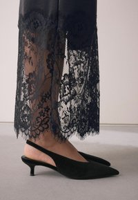 Svarta slingback-klackar med en mjuk mocka-yta, spetsig tå och en låg kitten-klack, kombinerat med en svart spetskjol med blommönster.