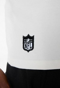 NFL-Logo-Patch auf einem weißen Baumwollhemd mit schwarzen Akzenten. Das Logo ist gestickt und hat eine schildförmige Form mit Sternen.