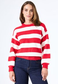 Rood en wit gestreepte trui met ribbelstructuur, ronde halslijn en lange mouwen, gecombineerd met donkerblauwe jeans.