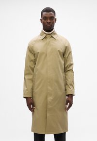 Beige waterdichte trenchcoat met een hoge kraag, raglanmouwen en zijzakken, voorzien van een gladde textuur en een minimalistisch ontwerp.