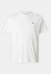 Camiseta de algodón blanca con mangas cortas, cuello redondo y un pequeño logo de cocodrilo bordado en verde en el lado izquierdo del pecho.