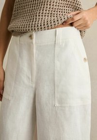 Leinenhosen in Off-White mit entspanntem Schnitt, ausgestattet mit Vordertaschen und einem Knopfverschluss in der Taille. Sichtbar strukturierter Stoff.