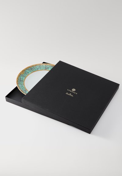 Διακοσμητικό πιάτο Versace, μερικώς τοποθετημένο σε μαύρο κουτί. Διαθέτει τιρκουάζ περίγραμμα με λεπτομερές χρυσό σχέδιο και καθαρό λευκό κέντρο.