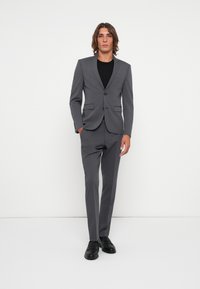 Gray suit made of smooth fabric, featuring a fitted blazer with two buttons and two front pockets, paired with matching trousers and black shoes.