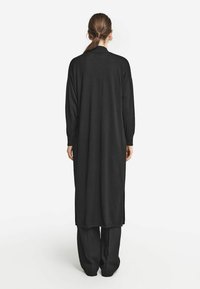 Czarny długi kardigan o prostym kroju, z długimi rękawami i bocznymi rozporkami, wykonany z miękkiego, lekkiego materiału.