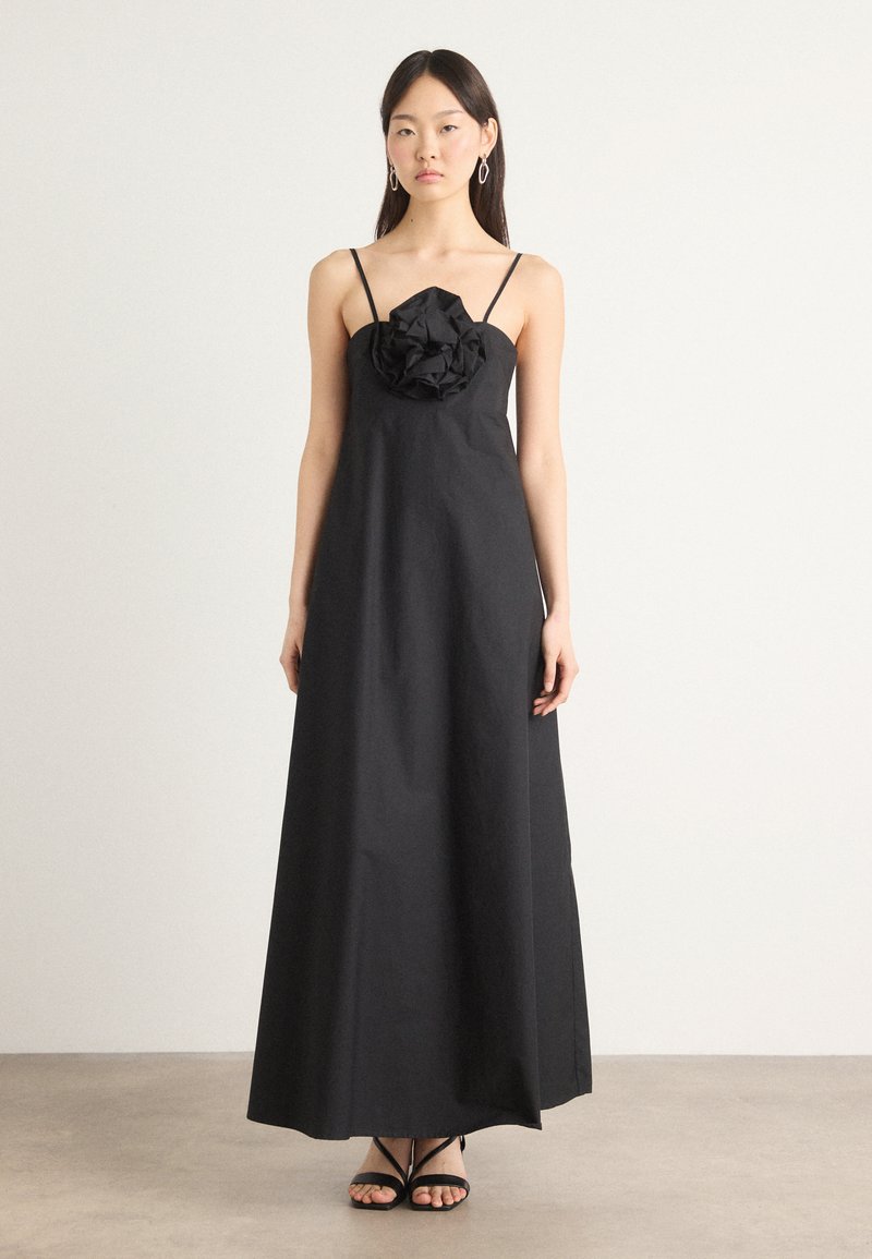Svart maxikjole med en tettsittende bodice og en teksturert blomsterdetalj ved brystet. Har tynne spaghettistropper og en glatt, flytende skjørt.
