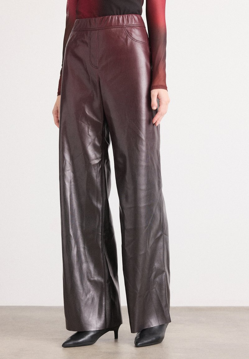 Pantalons en faux cuir bordeaux à jambes larges avec une texture lisse, une taille élastique et des coutures discrètes. Associés à des escarpins noirs à bout pointu.