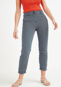 Pantaloni a righe navy e bianchi con vestibilità slim, orli arrotolati e vita con cintura. La texture liscia e il design sartoriale ne esaltano la struttura.