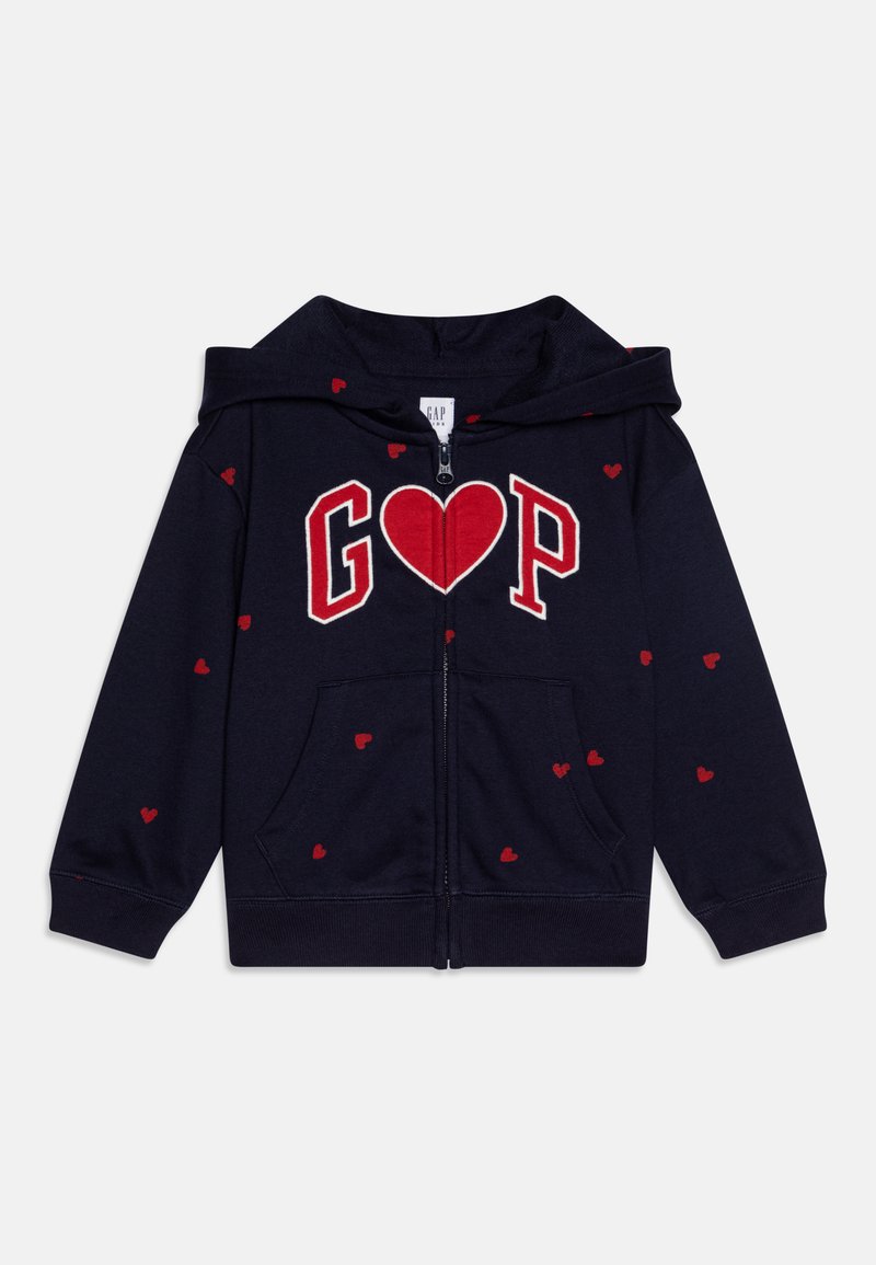 Sweatshirt com fecho éclair na cor azul-marinho, apresentando o gráfico "GAP" e um coração em vermelho. Pequenos corações vermelhos espalhados pelo tecido. Feito de material macio.