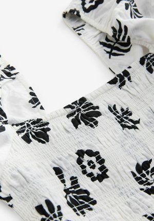 Črn cvetlični vzorec na belem lahkem blagu, ki vključuje smockiran pas in široke naramnice. Poudarite teksturirano in nabirano zasnovo.