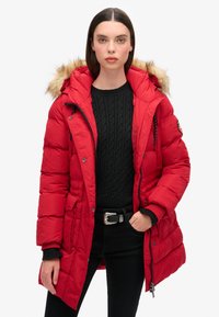 Chaqueta de plumas roja con capucha de piel sintética, cierre frontal con cremallera y bolsillos laterales. Presenta un diseño acolchado y puños acanalados para mayor calidez.