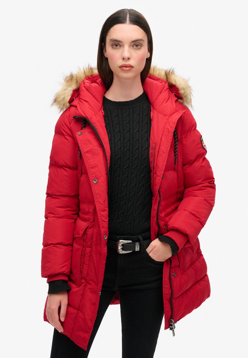 Chaqueta de plumas roja con capucha de piel sintética, cierre frontal con cremallera y bolsillos laterales. Presenta un diseño acolchado y puños acanalados para mayor calidez.