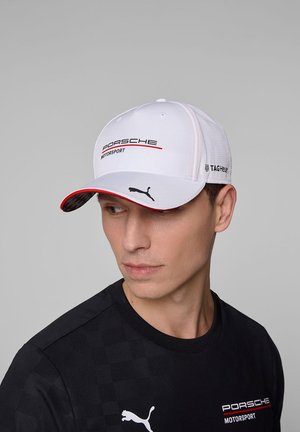 Biała czapka bejsbolowa z logo Porsche Motorsport, czerwonymi akcentami i czarnym kratkowanym wzorem na spodzie daszka. Logo Tag Heuer po bokach.