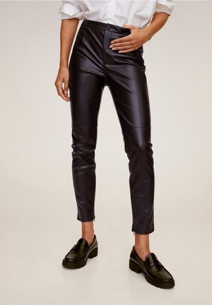 Schwarze Hose aus Kunstleder mit hoher Taille, figurbetontem Design, seitlichem Reißverschluss und glatter Textur, kombiniert mit schwarzen Slippern.