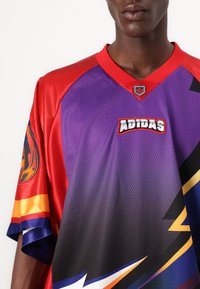 Red, purple, and black Adidas jersey with mesh texture, bold graphic design, contrasting colors, and logo at the neckline and sleeve.