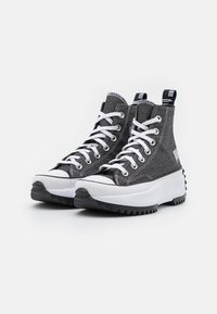 Höga sneakers med en grå denimöverdel, vita snören och gummidetaljer. Har en klumpig vit mellansula och mönstrad svart yttersula.