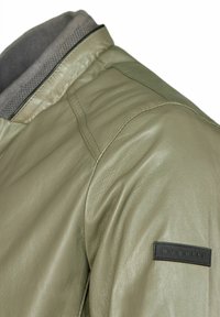 Olijfgroene leren bomberjack met een grijze binnencollier, voorzien van een gestructureerd zwart etiket op de linkerschouder. Vervaardigd met een gladde afwerking.