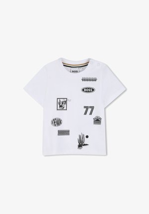 T-shirt blanc à manches courtes pour enfants, avec des imprimés graphiques noirs comprenant "BOSS", "77", un cactus, et le texte "IN THE MAKING", ainsi que des pressions à l'épaule.