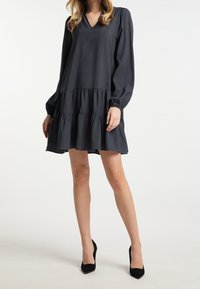 Dunkelgraues, knielanges Kleid mit langen puffädern Ärmeln, V-Ausschnitt und gestuftem Rüschendesign. Glattes Material mit einem fließenden Textur.