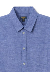 Camisa azul de manga corta hecha de tela texturizada con cuello abotonado, bolsillo frontal y botones de color gris claro. Etiqueta de OVS kids visible.