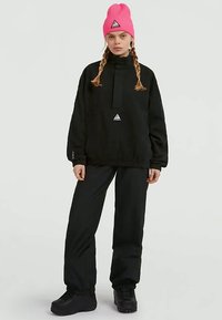 Felpa nera oversize con colletto alto, polsini elasticizzati e un piccolo logo triangolare. Abbinata a pantaloni neri e un berretto in maglia rosa brillante.