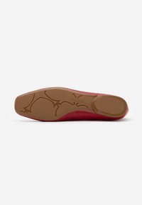 Semelle de chaussure rouge avec un fond en caoutchouc texturé de couleur beige, arborant un motif unique et une partie supérieure lisse de couleur rouge.