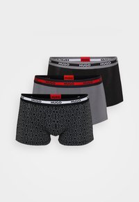 Tres pares de calzoncillos de hombre: uno negro con estampado, uno gris liso y uno negro liso, todos con cinturillas elásticas y detalles con logotipo.