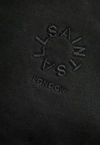 Tessuto nero con ricami testurizzati delle parole "SALTY" e "LONDON", circondato da un design a raggi di sole circolare. Finitura liscia e opaca.