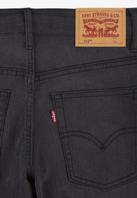 Jeans de mezclilla negra con un diseño distintivo en el bolsillo trasero, una etiqueta de pestaña roja y un parche de cuero marrón de la marca en la cintura.