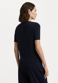 Σκούρο μπλε κοντομάνικο πουλόβερ με υφή λογότυπου. Διαθέτει στρογγυλή λαιμόκοψη και ριγωτό στρίφωμα, κατασκευασμένο από ελαφρύ πλεκτό υλικό.